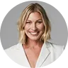 Professional headshot of a smiling woman in a white blazer against gray background